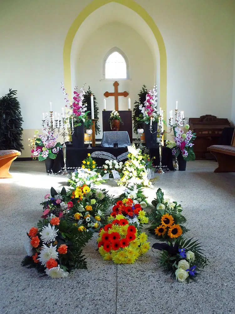 Blumen- und Kerzen-Arrangement vor einer Urne, in einer Kapelle